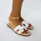 Elegante weiße Sandalen mit flachem Absatz und goldener Fußkette. Perfekt für Sommermode, Damenmode, stilvolle Schuhe, bequeme Sandalen.