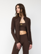 Frau in braunem Sportoutfit mit Reißverschlussjacke und Leggings, ideal für Fitness und Yoga. Modische Sportbekleidung für Damen.