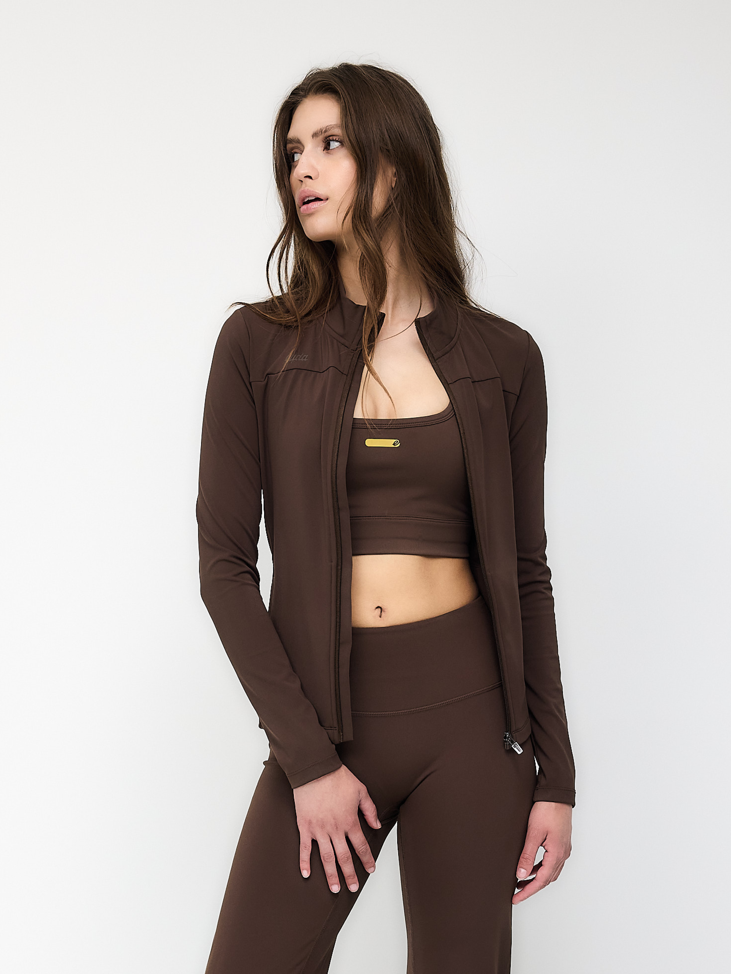 Frau in braunem Sportoutfit mit Reißverschlussjacke und Leggings, ideal für Fitness und Yoga. Modische Sportbekleidung für Damen.
