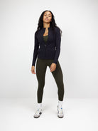 Schwarze Zip-Bluse für Damen, sportlich-elegant, ideal für Freizeit und Fitness. Kombiniert mit olivgrüner Leggings und weißen Sneakers.