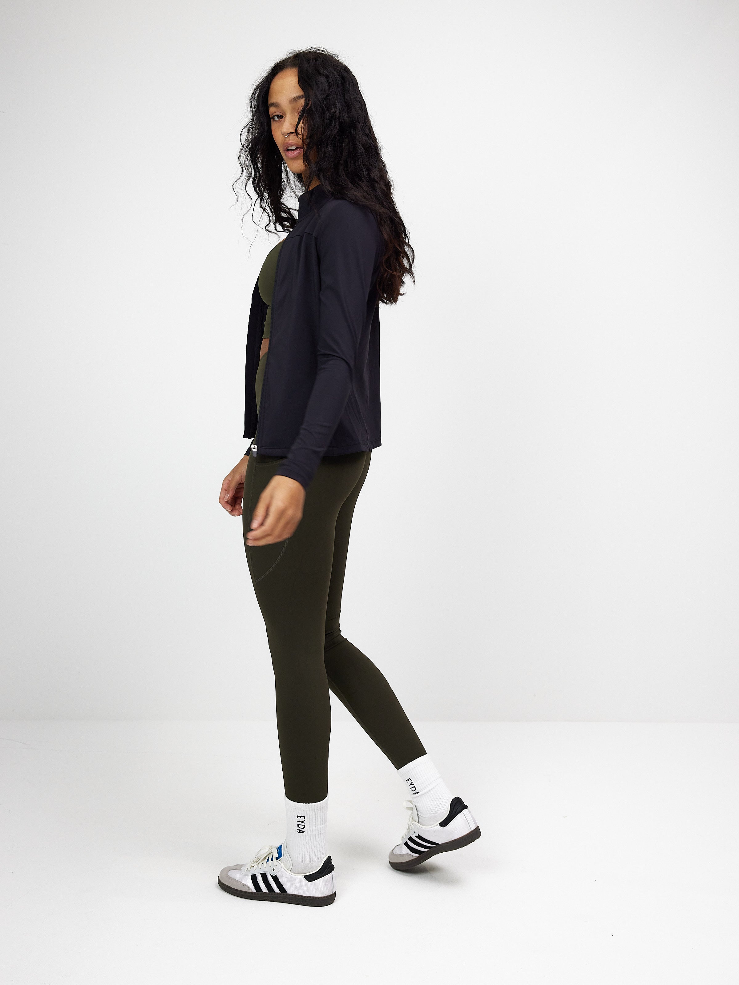 Schwarze Zip-Bluse für Damen, kombiniert mit olivgrüner Leggings. Perfekt für Sport und Freizeit. Modisch, bequem, vielseitig einsetzbar.
