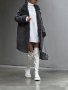 Damenmantel aus Lammwolle, lang und stilvoll, kombiniert mit weißen Overknee-Stiefeln und Strickkleid. Perfekt für modische Winteroutfits.