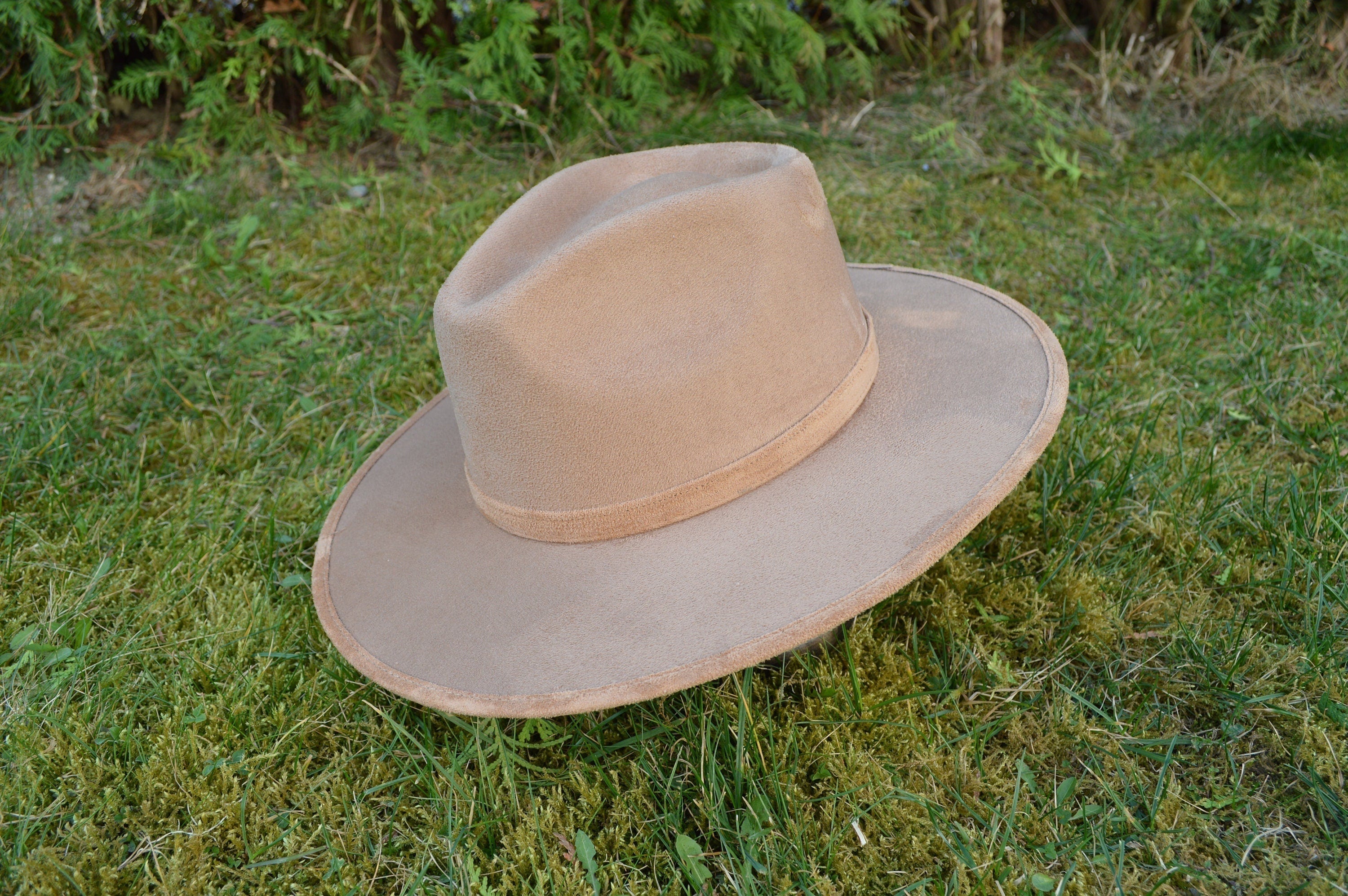 Breiter Cowboyhut aus braunem Wildleder auf grünem Gras. Perfekt für Westernmode, Outdoor-Abenteuer und stilvolle Accessoires.