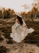 Frau in weißem Boho-Kleid und Hut in herbstlicher Landschaft, romantischer Stil, Natur, Mode, Outdoor-Fotografie, Vintage-Look.