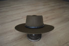 Brauner Filzhut mit breiter Krempe und schwarzem, genietetem Band auf Holzboden. Perfekt für Westernmode, stilvoll und zeitlos.