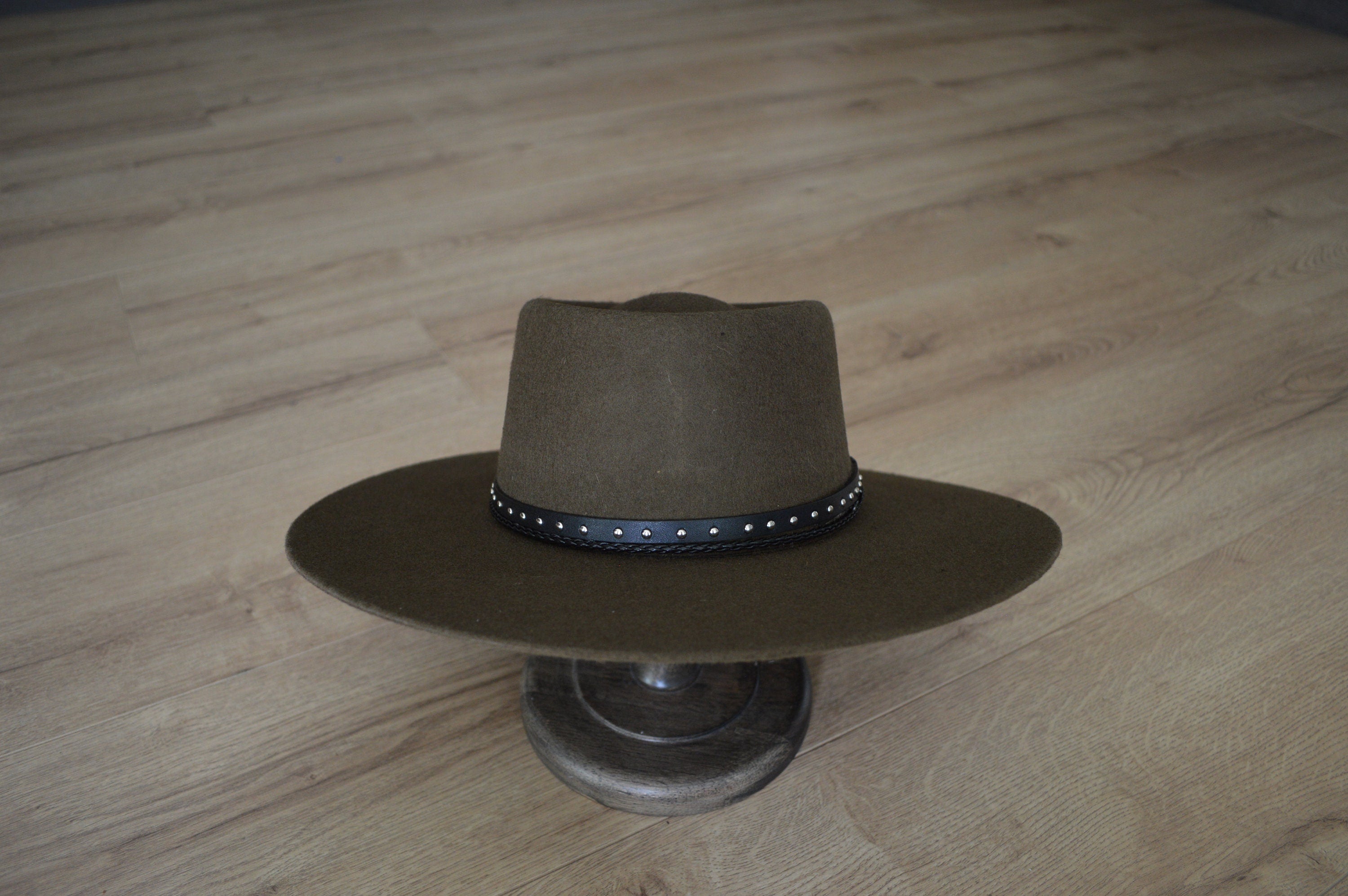 Brauner Filzhut mit breiter Krempe und schwarzem, genietetem Band auf Holzboden. Perfekt für Westernmode, stilvoll und zeitlos.