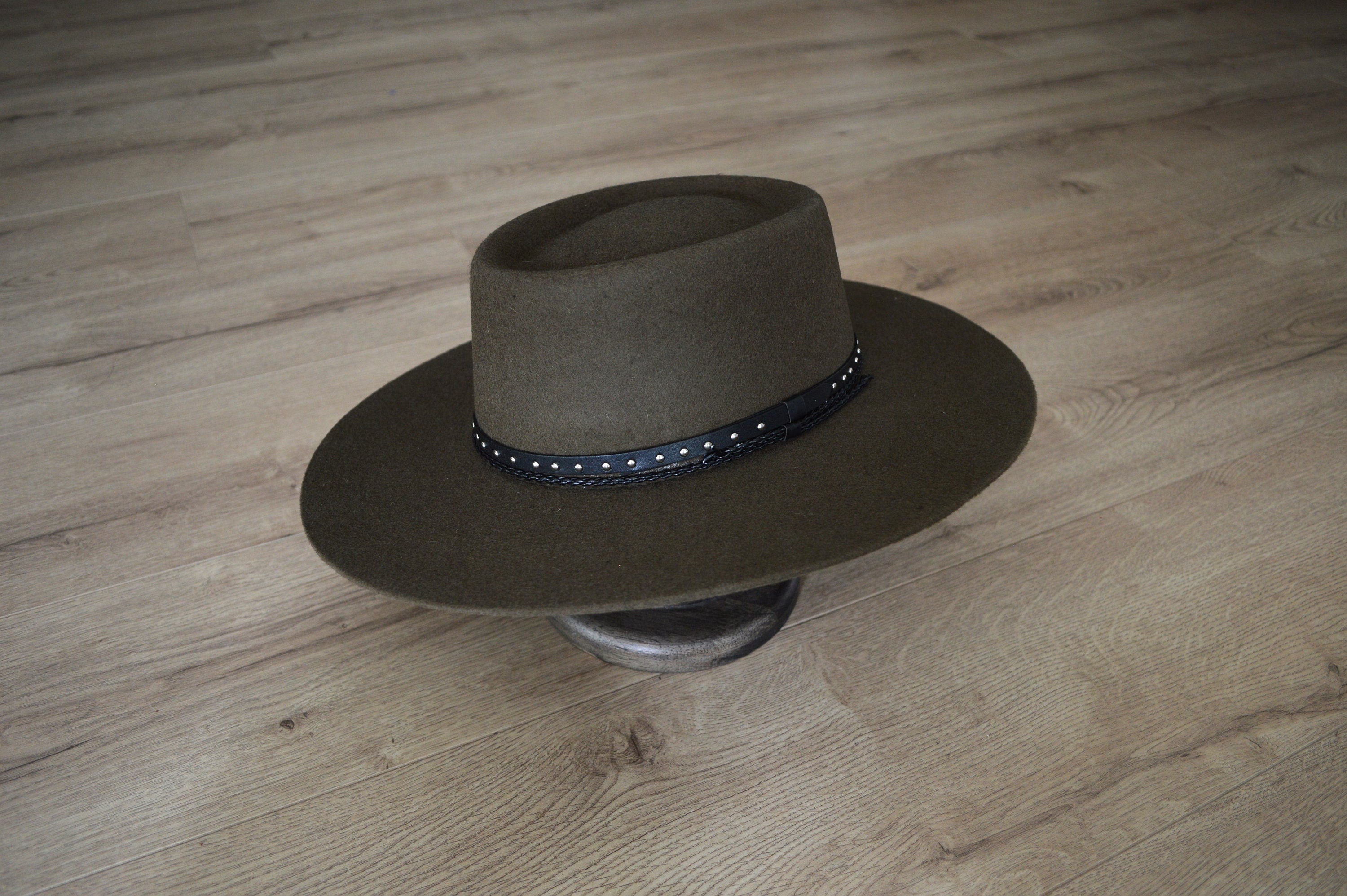 Brauner Filzhut mit breiter Krempe und schwarzem, verziertem Band auf Holzboden. Eleganter Westernhut, ideal für stilvolle Outfits.