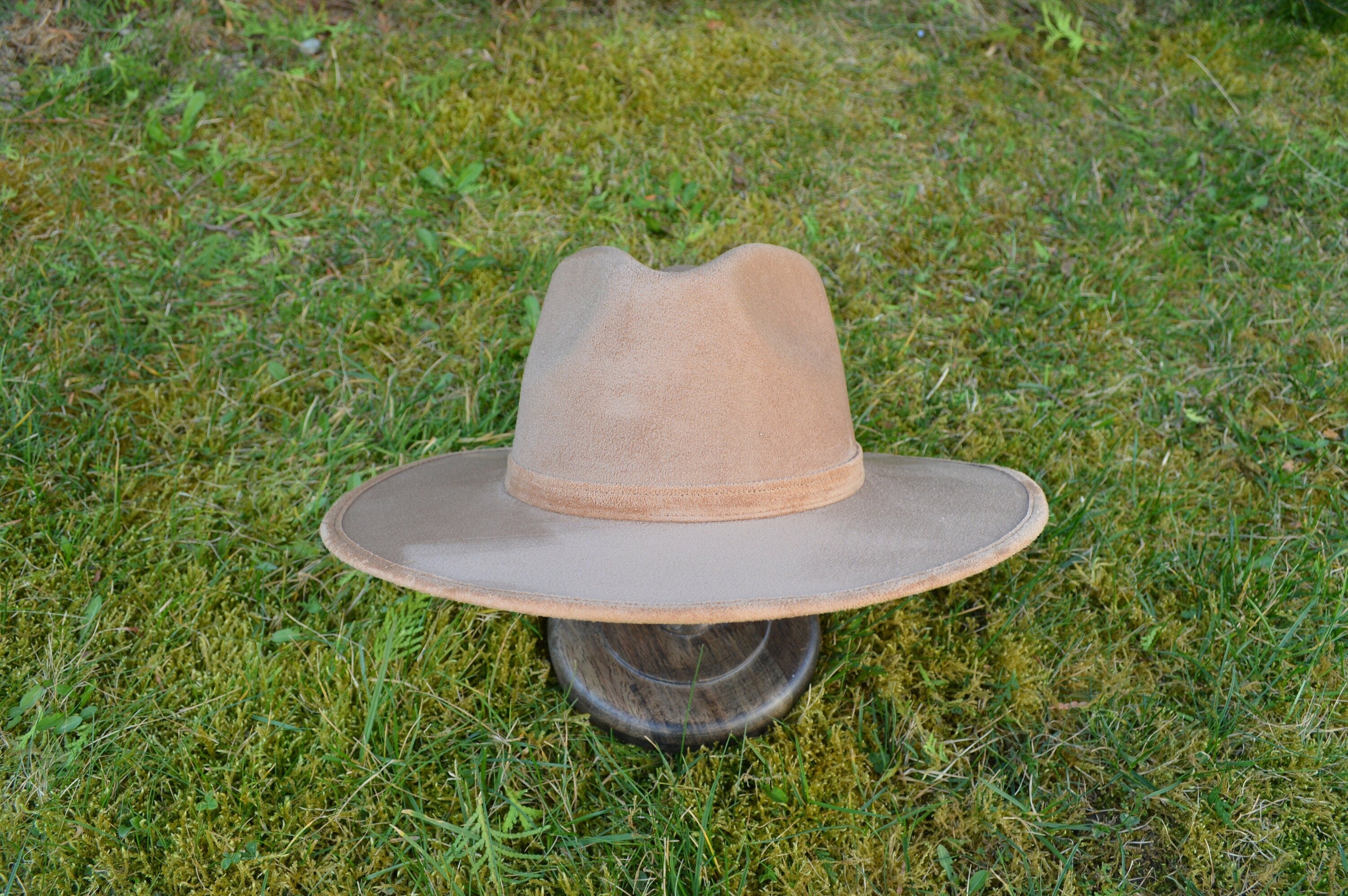 Beiger Cowboyhut aus Wildleder auf grünem Gras. Stilvoller Westernhut, ideal für Outdoor-Abenteuer und modische Akzente.
