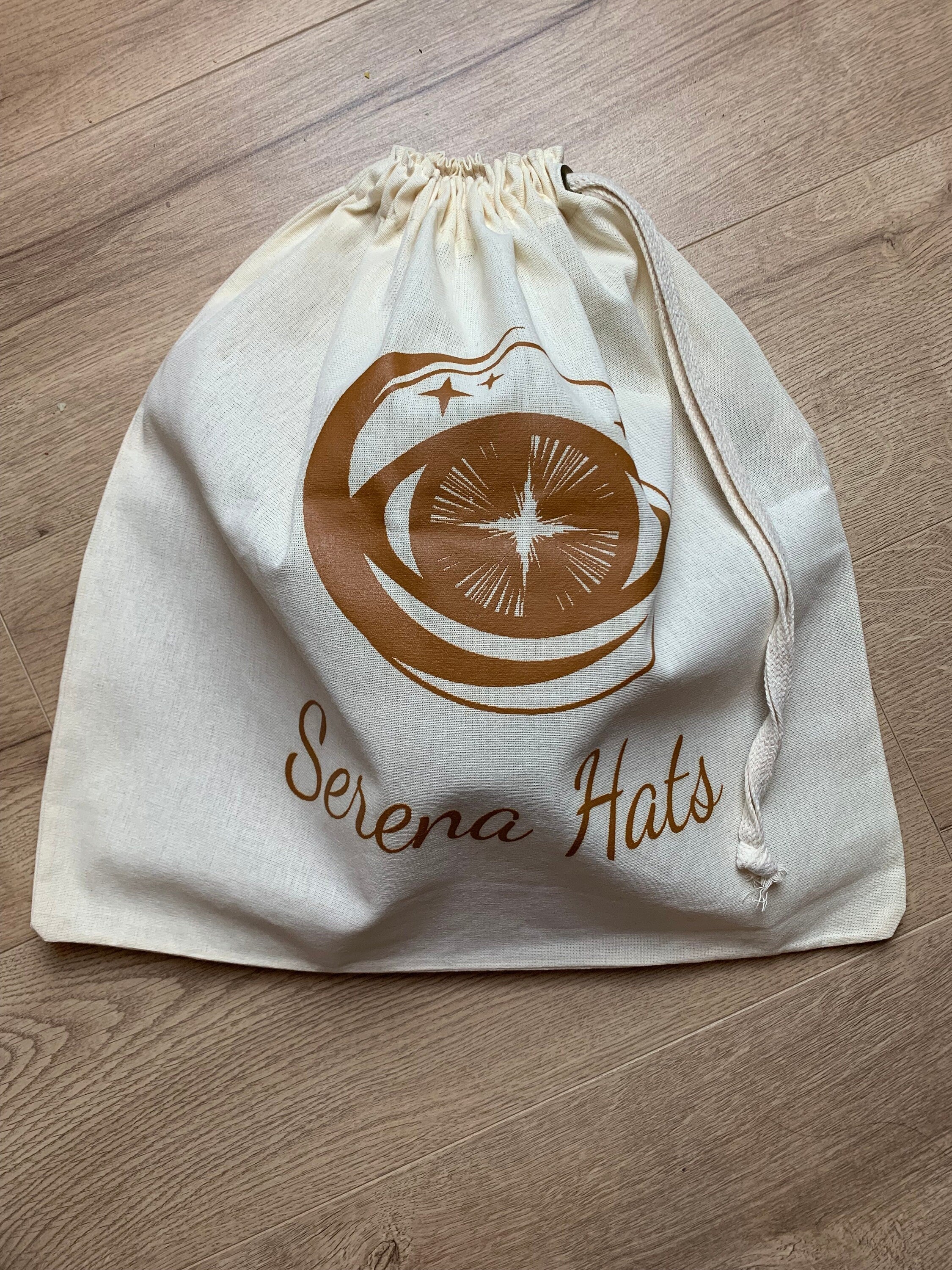 Baumwollbeutel mit Kordelzug, bedruckt mit "Serena Hats" Logo. Perfekt für umweltfreundliche Aufbewahrung und Transport von Hüten.