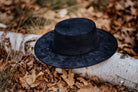 Schwarzer Filzhut auf Birkenstamm im Herbstlaub. Eleganter, breiter Rand, ideal für stilvolle Herbstmode. Hochwertige Handwerkskunst.