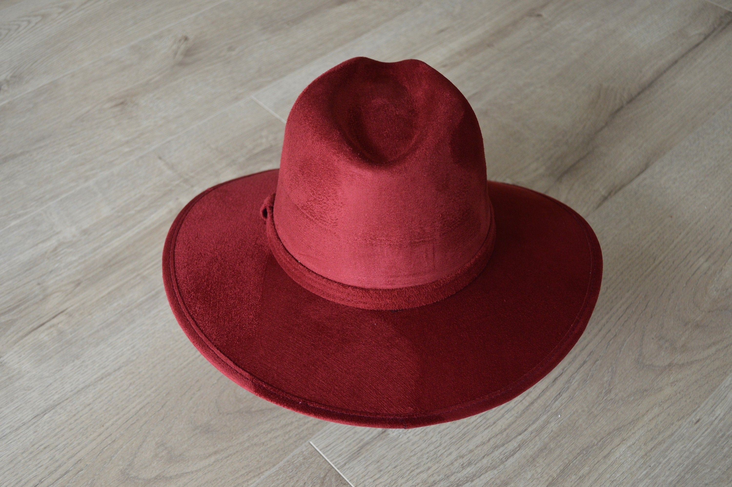 Roter Filzhut mit breiter Krempe auf Holzboden. Eleganter Damenhut, ideal für Herbstmode. Hochwertige Accessoires, stilvoll und zeitlos.