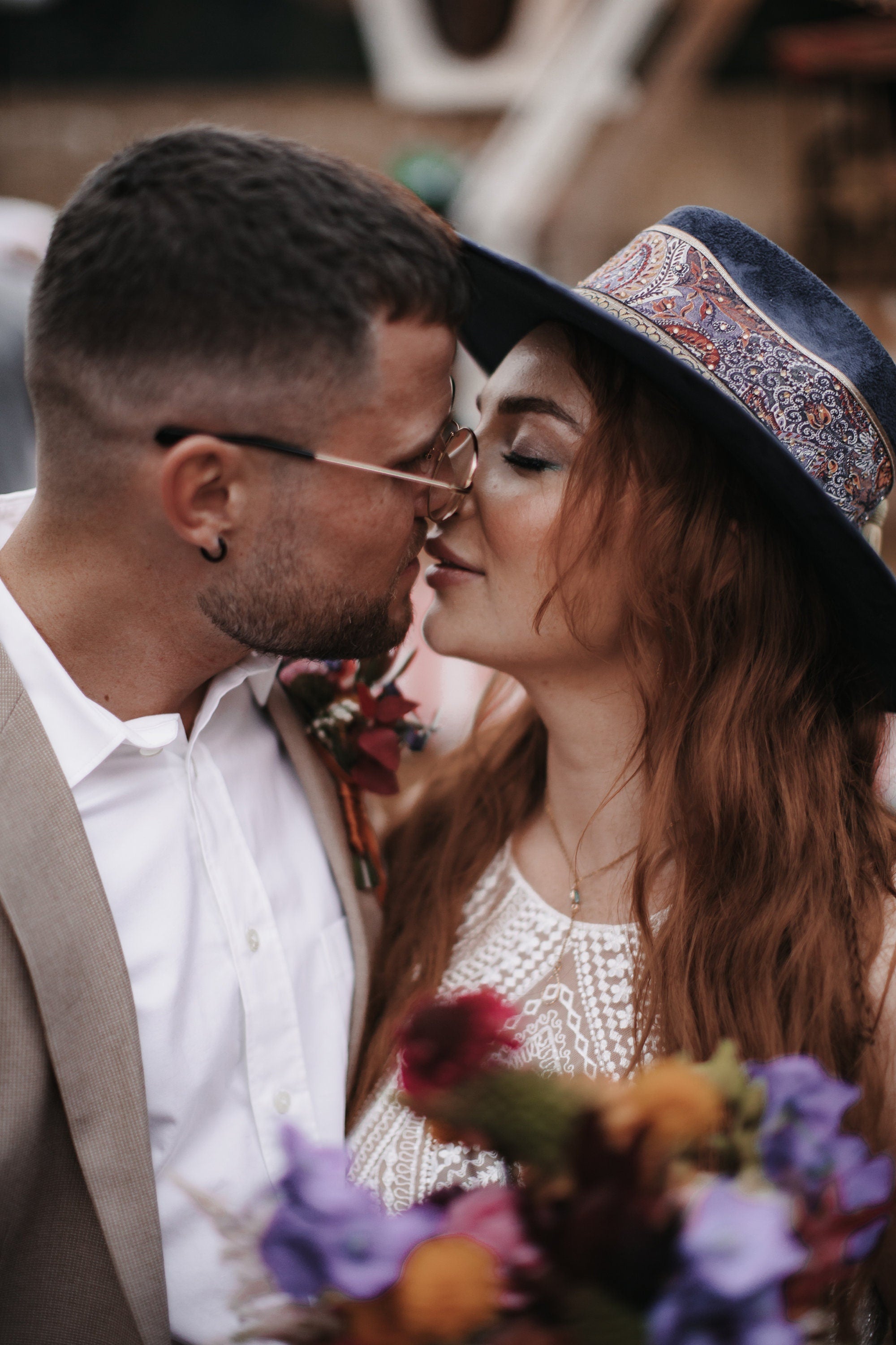 Paar in romantischem Moment, Mann im Anzug, Frau mit Hut und Blumenstrauß. Hochzeit, Liebe, Romantik, Brautpaar, Outdoor-Event, Boho-Stil.