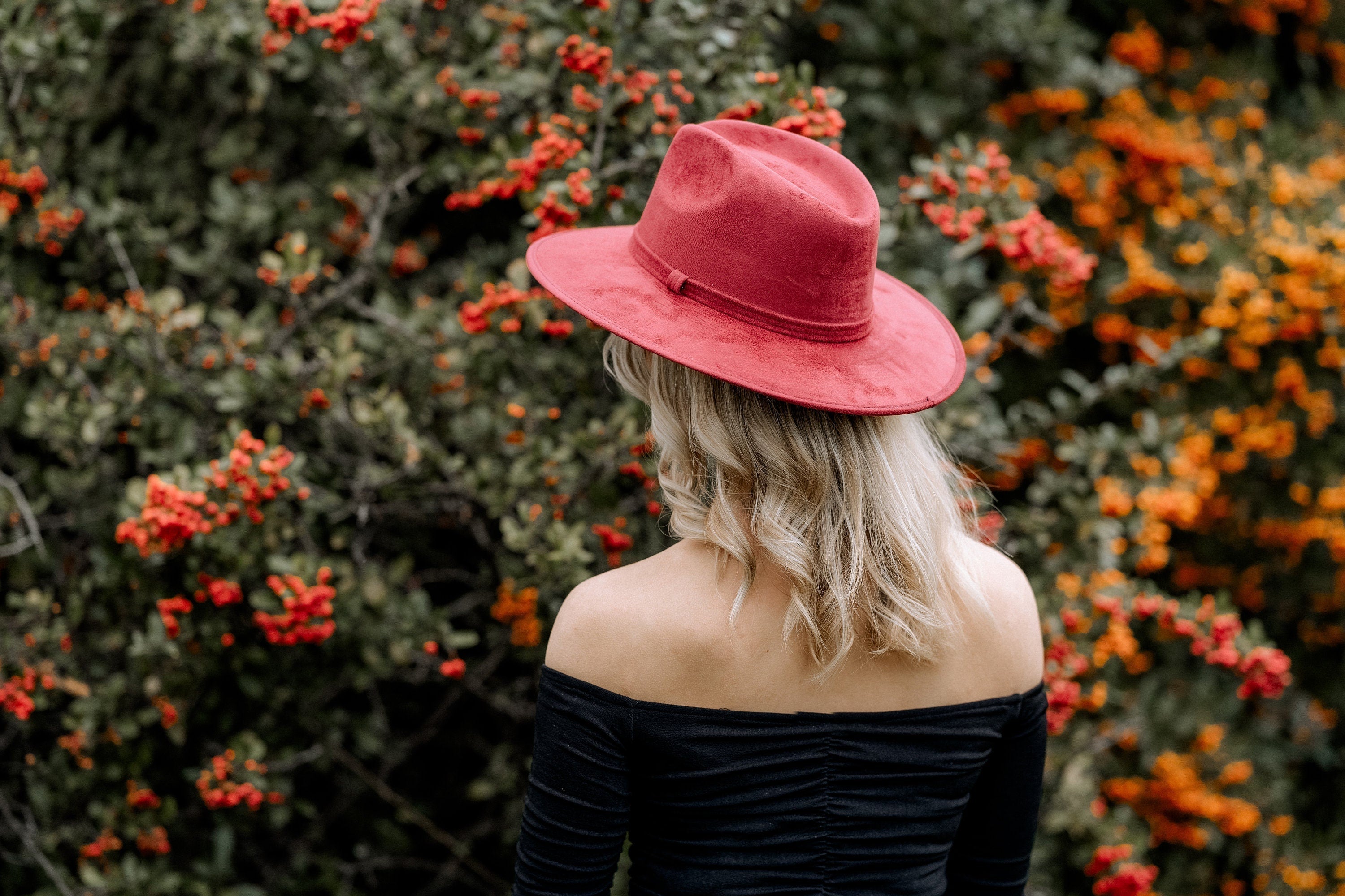 Frau mit rotem Hut vor Beerenstrauch, Herbstmode, stilvoll, Natur, Outdoor, Modeaccessoire, Damenhut, trendig, elegantes Outfit.