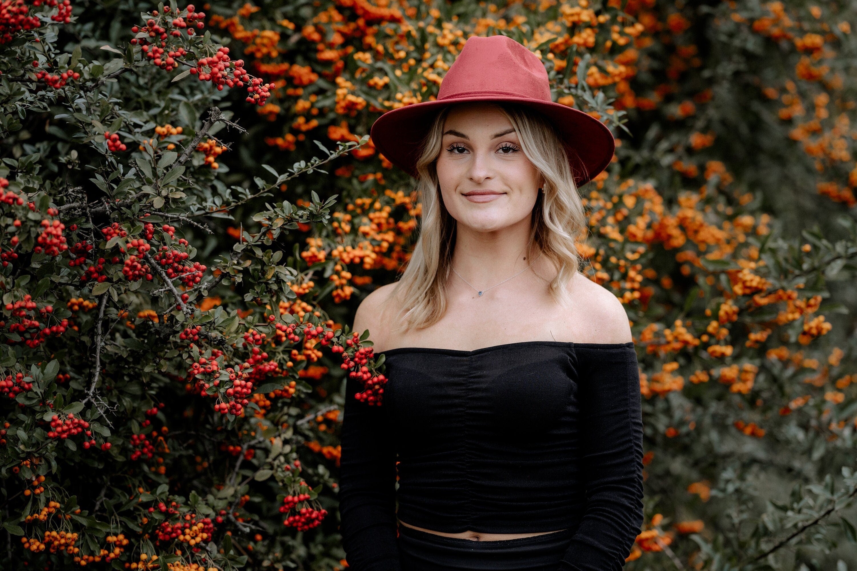 Frau mit rotem Hut vor herbstlichem Hintergrund aus roten und orangefarbenen Beeren. Mode, Herbst, Outdoor, stilvoll, Naturfotografie.