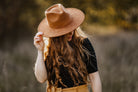 Frau mit langem, lockigem Haar trägt braunen Fedora-Hut im Freien. Modetrend, Herbstmode, stilvoller Look, Damenhut, Naturhintergrund.