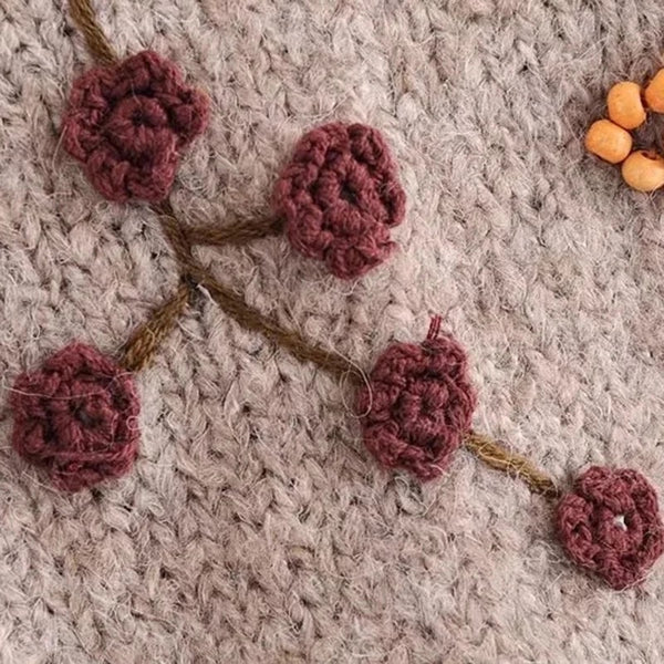 Handgestrickter Wollpullover mit floralen Häkelmustern, beige Hintergrund, warme Herbstfarben, einzigartiges Design, gemütliche Mode.