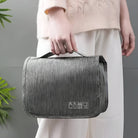 Graue Kulturtasche aus Stoff, tragbar, mit Griff, ideal für Reisen, Kosmetikaufbewahrung.