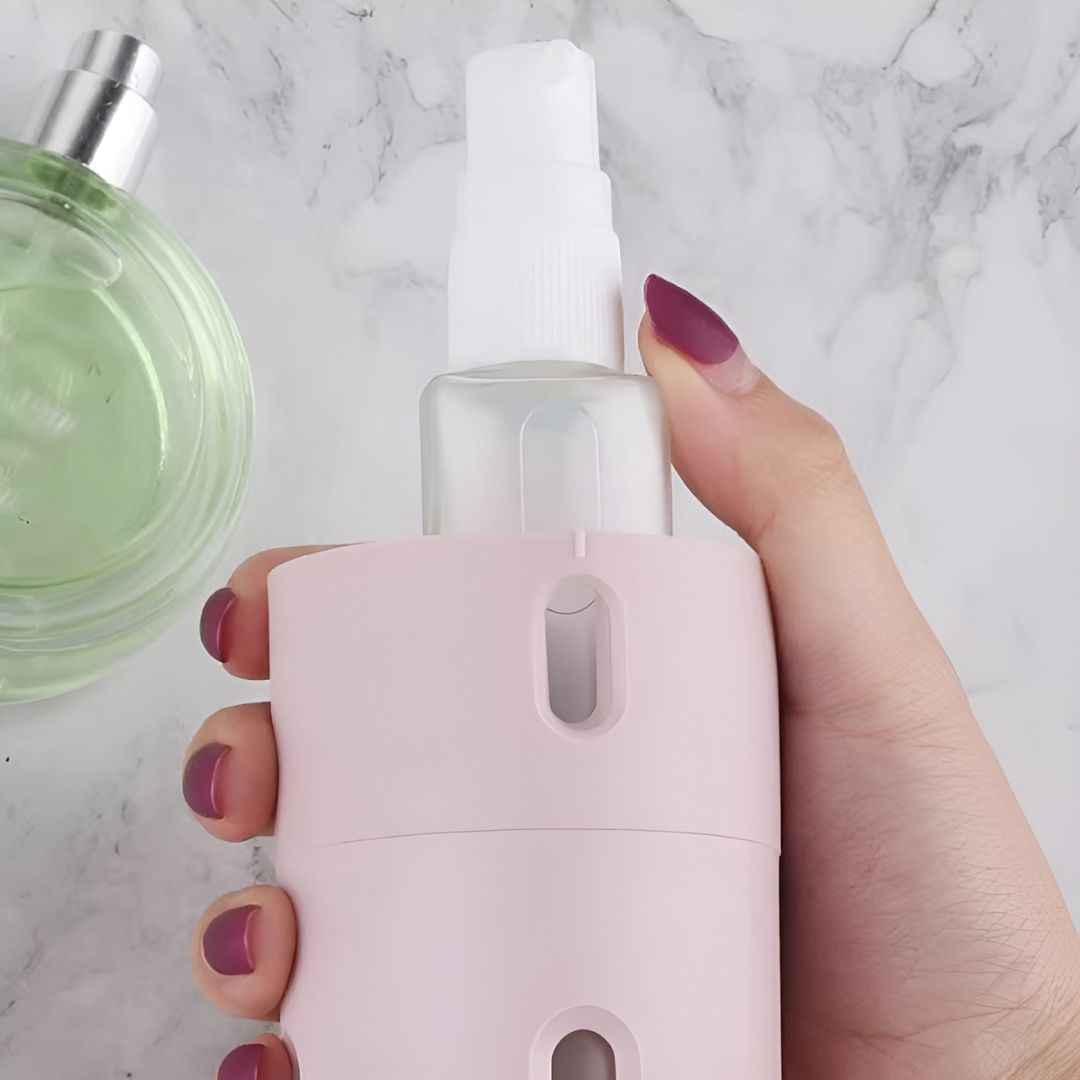 Hand hält rosa Sprühflasche auf Marmorhintergrund, Parfümflakon im Hintergrund.