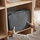 Graue Aufbewahrungstasche aus Stoff im Regal, platzsparend, ideal für Kleidung und Accessoires.
