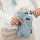 Person hält hellblaue Umhängetasche mit Smartphone und Flasche, modisches Accessoire.