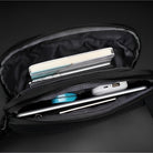 Schwarze Umhängetasche mit Fächern, enthält Notizbuch, Stift, Ladegerät und Kabel, ideal für Reisen.