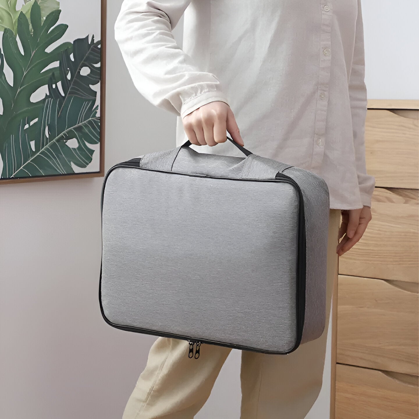 Person hält graue, tragbare Aufbewahrungstasche mit Reißverschluss, ideal für Reisen und Organisation.