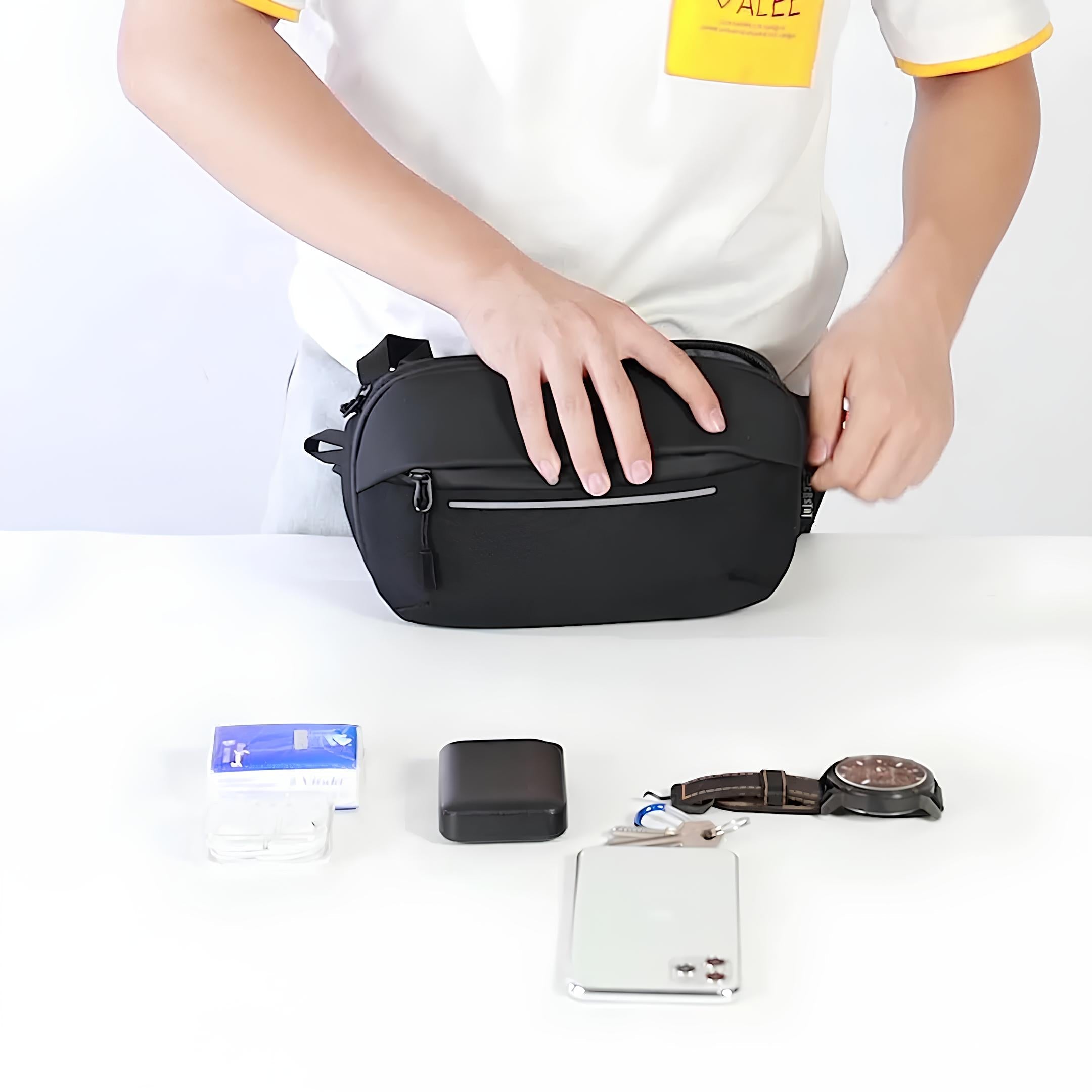Mann packt schwarze Umhängetasche, umgeben von Uhr, Smartphone, Ladegerät und Kartenetui.
