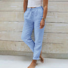 Frau in hellblauer Leinenhose, lässig, bequem, Sommermode, vor Holzwand stehend.