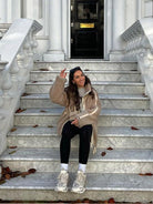 Frau in beiger Winterjacke auf Marmortreppe, lässig sitzend. Herbstmode, stilvolle Damenbekleidung, Outdoor-Look, urbane Eleganz.