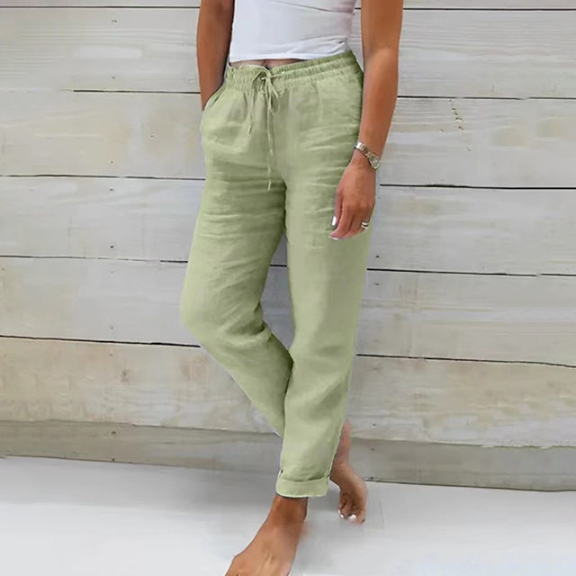 Frau in hellgrüner Leinenhose, weißem Top, lässiger Look, Sommermode, Holz-Hintergrund.