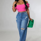 Frau in modischer Kleidung: pinkes Off-Shoulder-Top, zerrissene Jeans, grüne Clutch. Trendige Damenmode, lässiger Look, Streetstyle.