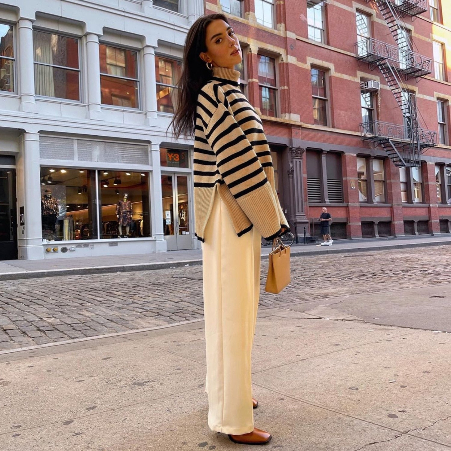 Damenmode: Gestreifter Pullover für Herbst/Winter, kombiniert mit eleganter weißer Hose. Perfekt für stilvolle, urbane Outfits in der kalten Jahreszeit.