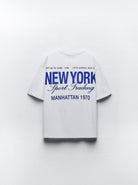 Weißes T-Shirt mit blauem "New York Sport Trading" Aufdruck, Manhattan 1970. Perfekt für lässige Mode, inspiriert von urbanem Stil.
