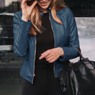 Frau in blauer Lederjacke, hält schwarze Handtasche. Modetrend, Damenbekleidung, stilvolle Jacke, Accessoires, urbane Mode.