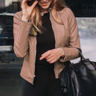 Frau in brauner Lederjacke, hält schwarze Handtasche. Modetrend, stilvolle Damenbekleidung, urbane Mode, Herbstoutfit.