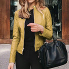 Frau in gelber Lederjacke und schwarzem Outfit, hält schwarze Handtasche. Modetrend, stilvolle Damenbekleidung, urbane Eleganz.