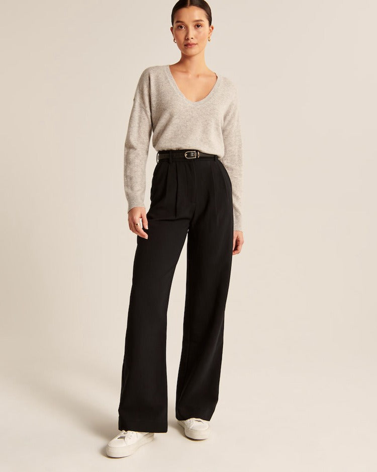 Eleganter Damen-Look: Grauer Pullover mit V-Ausschnitt, schwarze High-Waist-Hose, weiße Sneaker. Perfekt für stilvolle Freizeitmode.