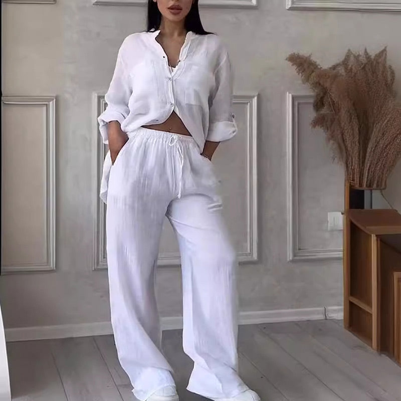 Frau in weißem Leinen-Set, bestehend aus lockerem Hemd und Hose, steht in modernem Interieur. Keywords: Damenmode, Leinenkleidung, Sommeroutfit.