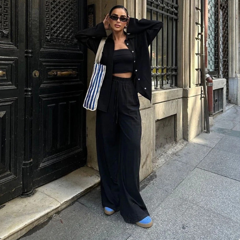 Stylische Frau in schwarzem Outfit mit gestreifter Tasche, posiert vor antiker Tür. Modetrend, Streetstyle, urbane Mode, lässiger Look.