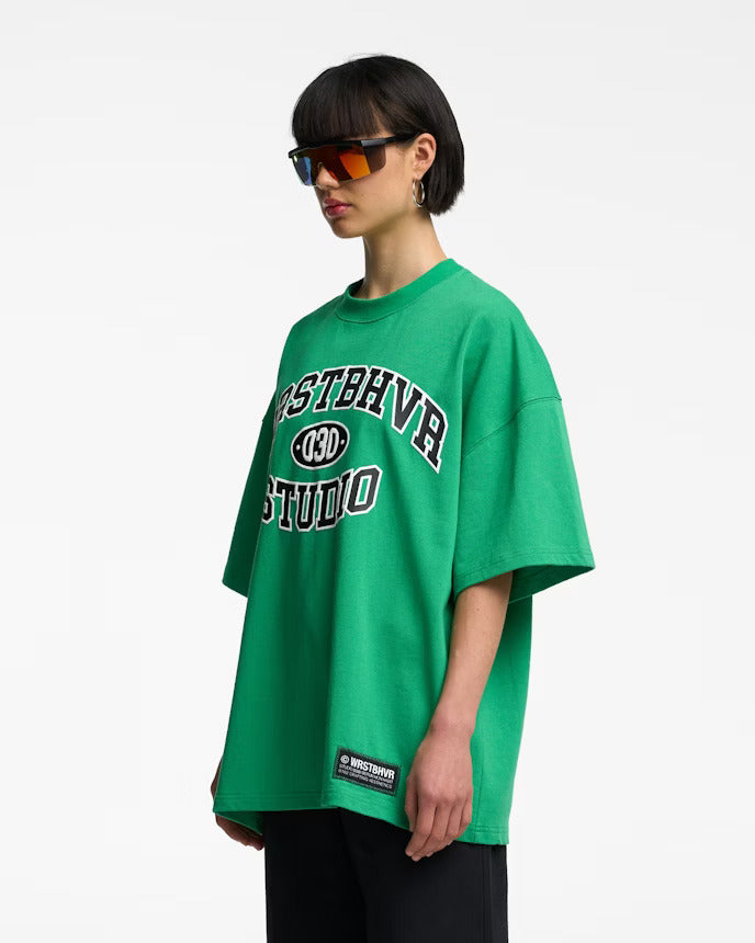Grünes Oversize-T-Shirt mit "Osthrav Studio" Aufdruck, getragen von Person mit Sonnenbrille. Trendige Streetwear, lässiger Stil, Unisex-Mode.