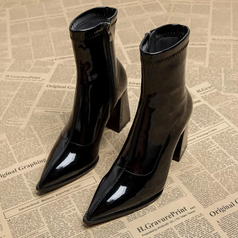 Schwarze Lackleder-Stiefeletten mit spitzer Zehenpartie und Blockabsatz auf Zeitungshintergrund. Modische Damenstiefel, elegant und trendig.