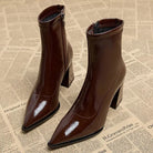 Braune Lackleder-Stiefeletten mit spitzer Zehenpartie und Blockabsatz auf Zeitungshintergrund. Modische Damenstiefel, elegant und trendig.