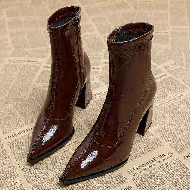 Braune Lackleder-Stiefeletten mit spitzer Zehenpartie und Blockabsatz auf Zeitungshintergrund. Modische Damenstiefel, elegant und trendig.