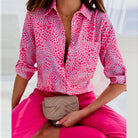 Damenbluse mit Umlegekragen in leuchtendem Pink und Herzmuster, kombiniert mit pinker Hose. Modetrend, stilvoll, auffällig.