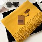 Gelber Schal mit Fransen aus weichem Material, stilvoll präsentiert neben Sonnenbrille. Perfekt für Herbstmode. Hochwertige Accessoires.