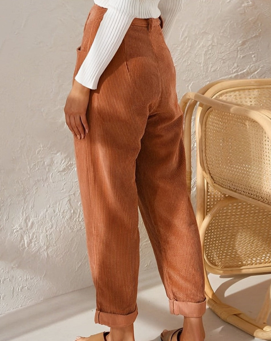 Frau in brauner Cordhose, weißem Pullover, Rattan-Stuhl, modisch, lässig, Herbstmode.
